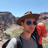 A person wearing a hat and sunglasses with a mountain in the background

Description automatically generated